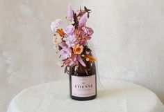 a bottle filled with flowers sitting on top of a white tablecloth covered stool next to a wall