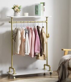 a rack with clothes hanging on it next to a chair and table in a room