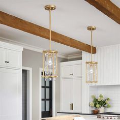 a kitchen with white cabinets and an island that has two pendant lights hanging from the ceiling