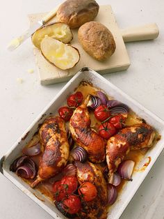 chicken and vegetables in a pan on a table with bread, potatoes and fruit next to them