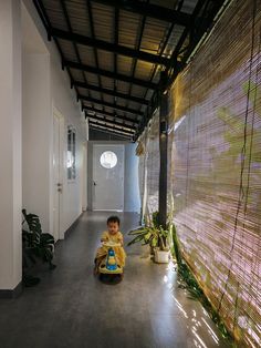 a small child sitting on the floor in front of a wall with bamboo blinds and plants