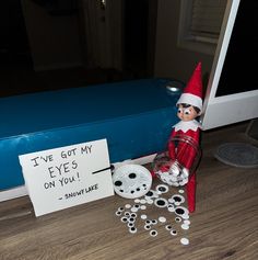 an elf is sitting on the floor next to a sign that says i've got my eyes on you