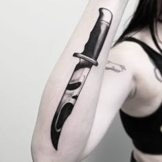 a woman with a knife tattoo on her arm, holding a knife in the other hand