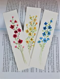 three bookmarks with flowers painted on them sitting on top of an open book page