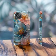 a phone case with flowers on it sitting on a wooden table next to a pen