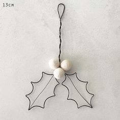 a metal holly ornament with two white balls hanging from it's side