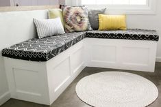 a white bench with pillows on it in front of a window and a round rug