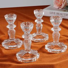 four clear glass candlesticks sitting on top of a brown cloth next to a book