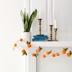 an orange garland is hanging on the mantle next to a potted plant and candles