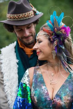 a man and woman dressed up in colorful clothing with feathers on their head looking at each other