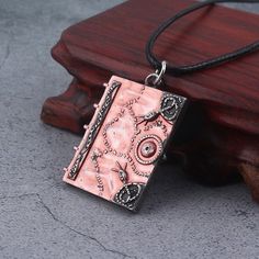 a pink necklace with an intricate design on the front and back of it, hanging from a wooden stand