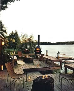 an outdoor deck with chairs, tables and fire pit on the water's edge