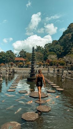 a woman is walking across stepping stones in the water