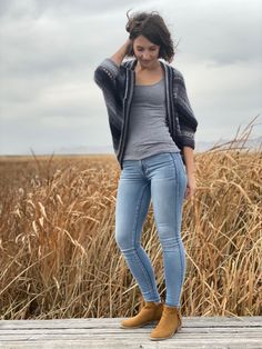 a woman standing on top of a wooden platform in front of a field with tall grass