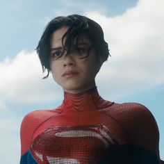 a young boy wearing a superman costume in front of a cloudy blue sky with clouds