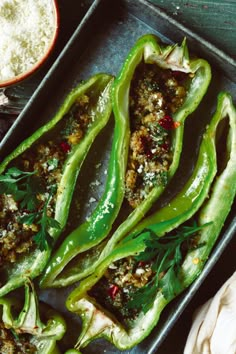 some green peppers are sitting on a pan with seasoning next to it and two bowls