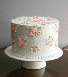 a white cake with pink flowers on it sitting on top of a wooden table in front of a gray wall