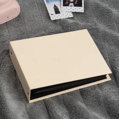 an open box sitting on top of a bed next to two polaroid pictures and a pink alarm clock