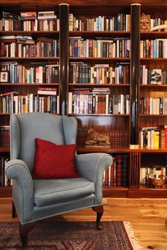 a chair with a red pillow in front of a book shelf filled with books and other books