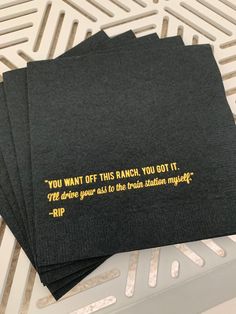 four black napkins with gold foil on them sitting on a table top next to each other