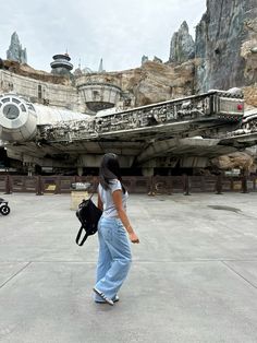 a woman with a backpack walking in front of a star wars ship