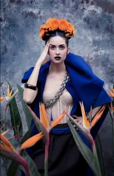 a woman with orange flowers in her hair is posing for the camera while wearing a blue cape