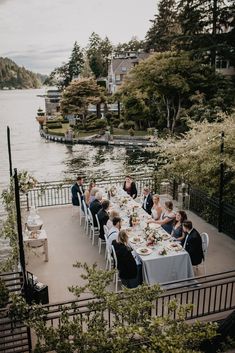 a group of people sitting around a table on top of a deck next to water