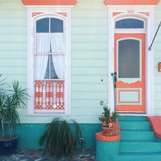 an orange and blue front porch with potted plants next to the door, on a sunny day