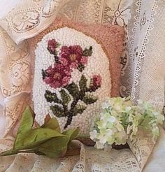 a white pillow with flowers on it next to a green leafy plant and lace