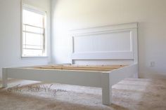 a white bed frame in a room with carpeted flooring and two windows above it