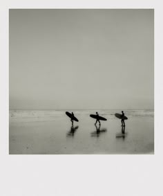 three people with surfboards walking on the beach