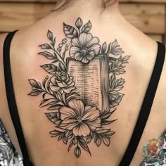 a woman's back tattoo with flowers and an open book