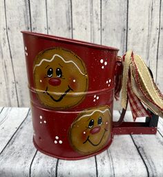 two red christmas mugs with faces painted on them, one has a gold ribbon