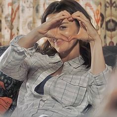 a woman sitting on top of a couch holding her hands up to her face and making a heart shape