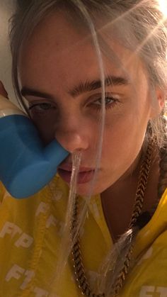 a woman drinking from a blue bottle while wearing a yellow shirt and braided hair