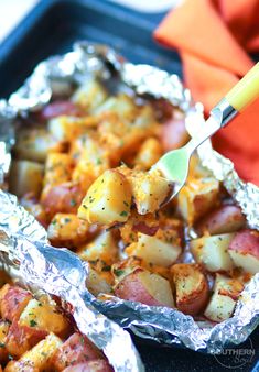 the potatoes are being cooked in foil with a spatula and orange napkin on the side