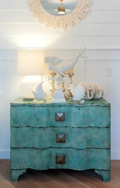 a blue dresser with shells on top and a mirror above it in a white room