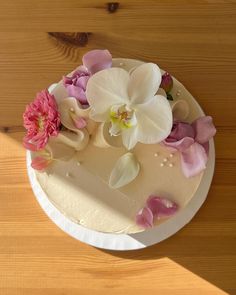 a white cake with pink and white flowers on the top is sitting on a wooden table