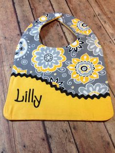 a baby bib with yellow and gray flowers on it, sitting on a wooden floor