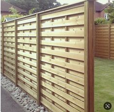 a wooden fence in the middle of a yard with rocks on the ground and grass behind it