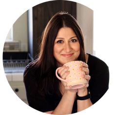 a woman holding a pink coffee cup in her right hand and smiling at the camera