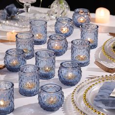 a table topped with lots of blue glass cups and saucers filled with lit candles