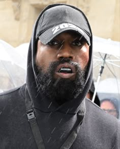 a man wearing a hoodie and holding an umbrella in the rain with other people behind him