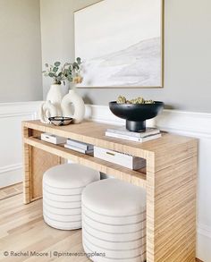 a wooden table with two stools and a bowl on it in front of a painting