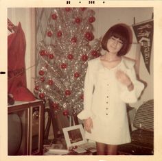 an old photo of a woman standing in front of a christmas tree