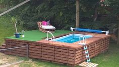 an above ground pool surrounded by wooden pallets and green grass with a ladder leading up to it