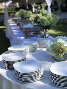 white plates are lined up on a table with flowers in vases and napkins