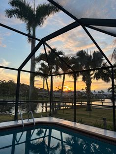 an outdoor swimming pool with palm trees and the sun setting in the distance behind it