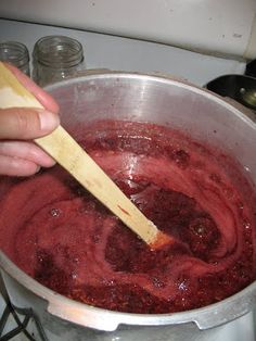 a person stirring red liquid in a pot with a wooden spoon on the stove top