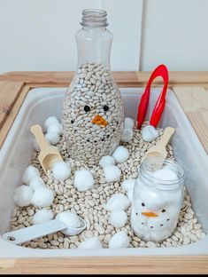 a snowman made out of rocks and plastic spoons sitting in a container filled with cotton balls